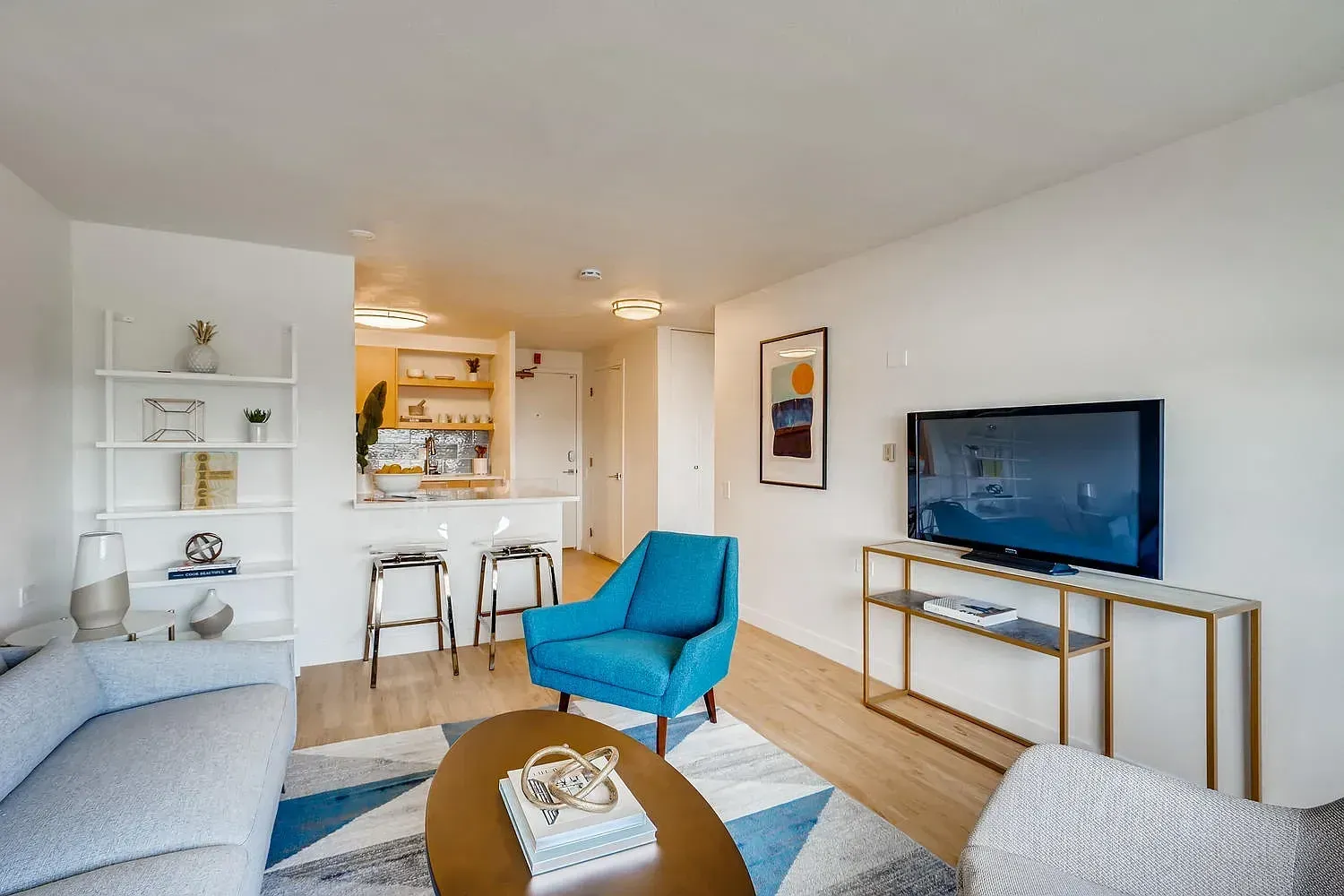 Modern living room with blue chair, TV, sofa, and a small kitchen bar in the background