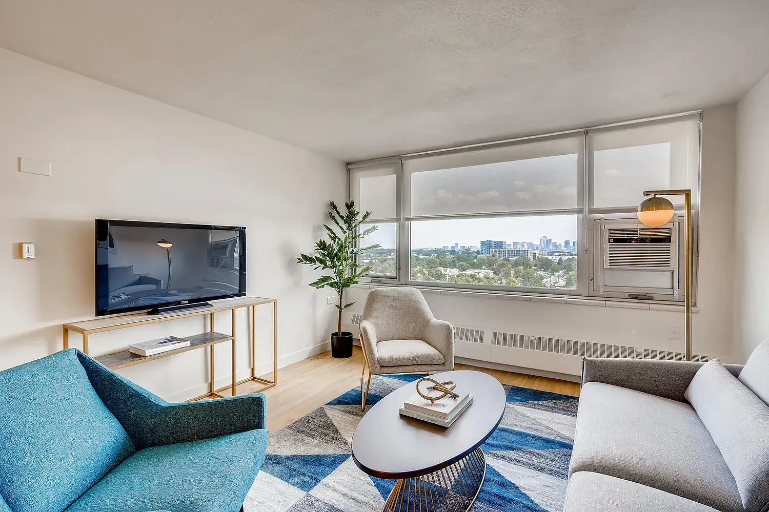 Bright living room with blue sofa, TV, coffee table, and large window city view
