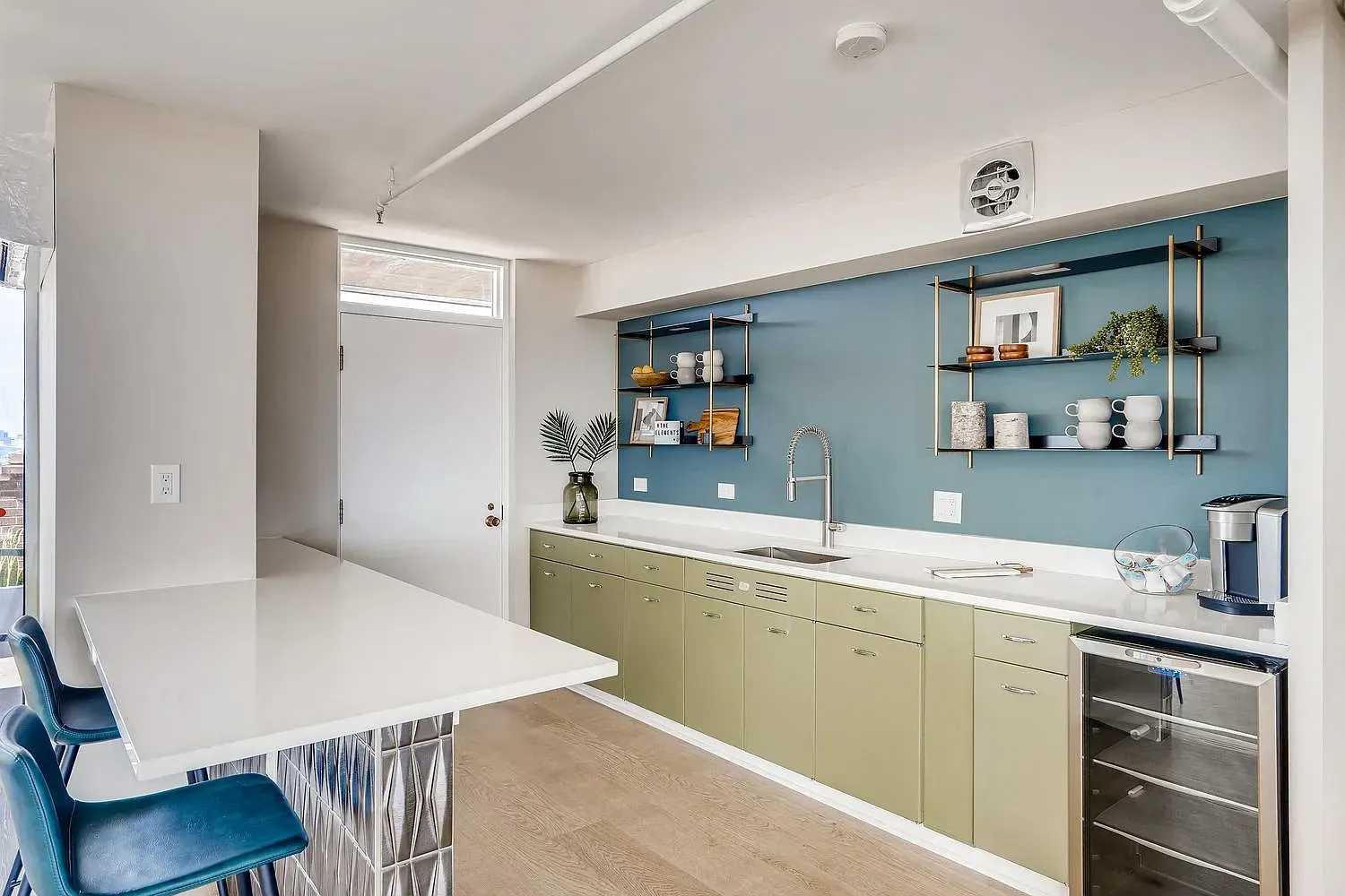 Modern kitchen with blue backsplash, green cabinets, white island, and bar stools