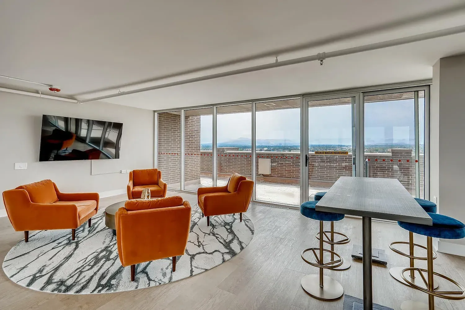Modern living room with orange chairs, white rug, and large windows overlooking a city view