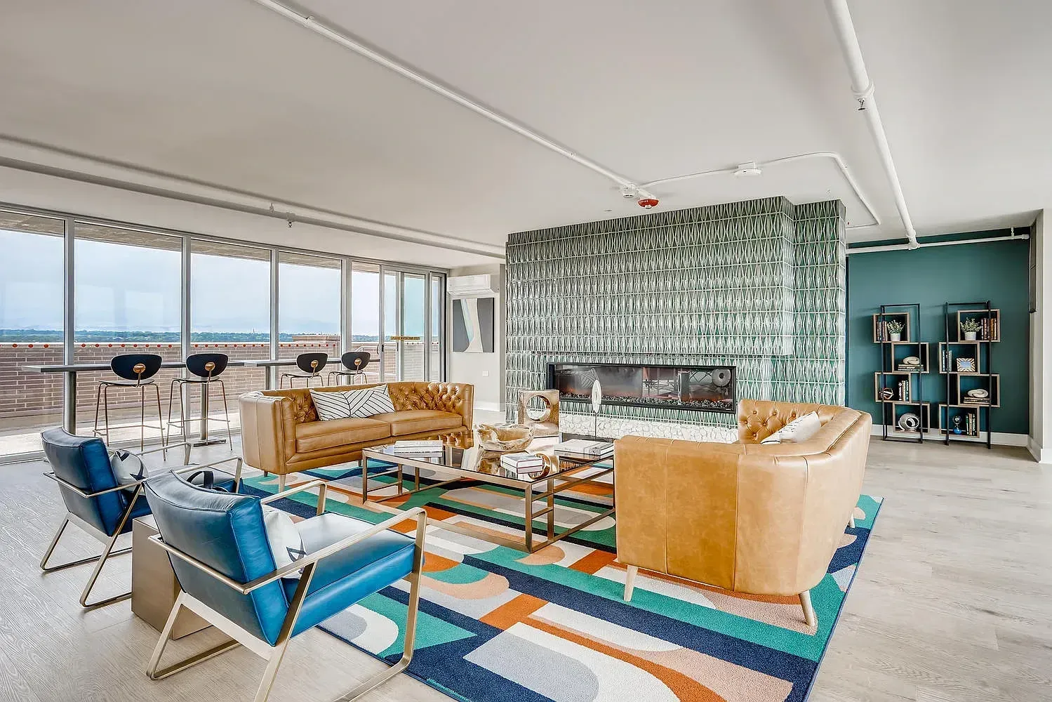 Bright modern living room with blue chairs, tan sofas, patterned rug, and city-view windows