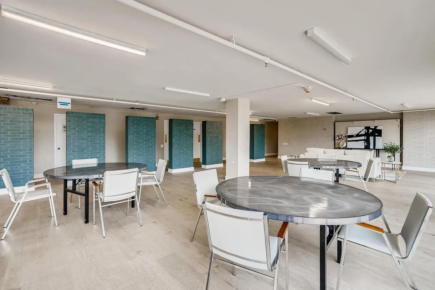 Bright modern lounge with round tables, white chairs, and wall-mounted TVs under fluorescent lights
