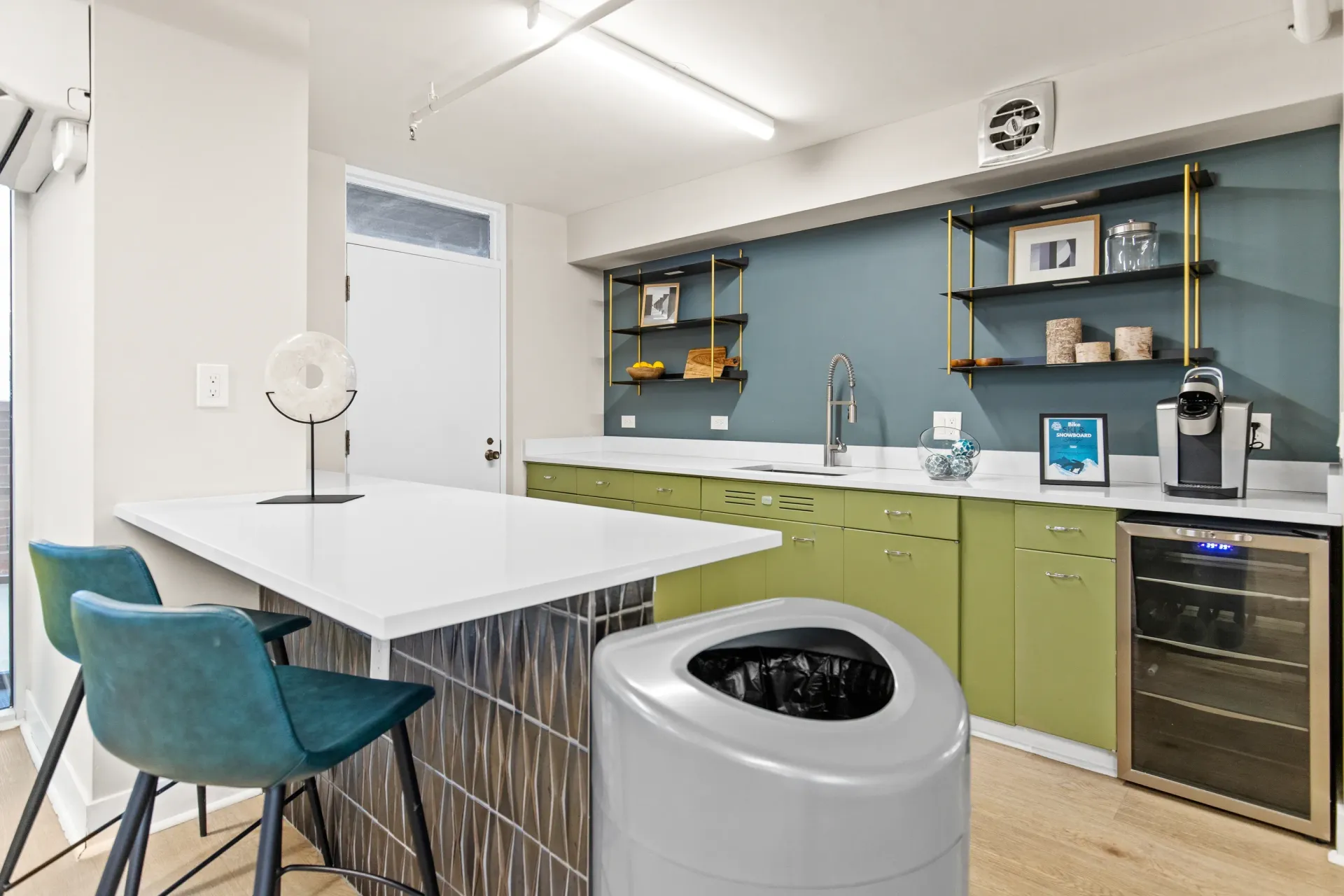 Kitchenette with island seating and modern green cabinetry.