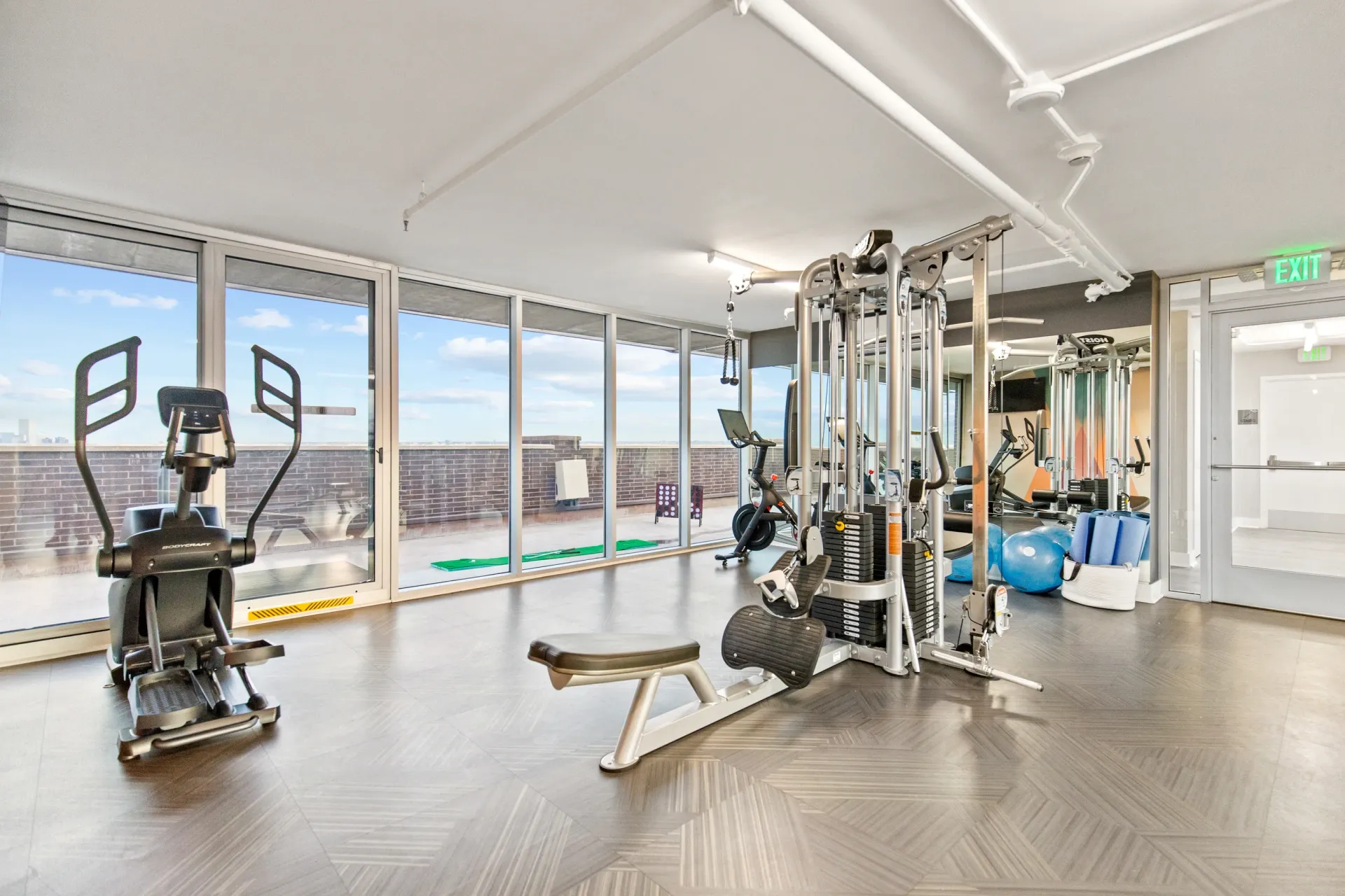 Gym with cardio machines, weight machines, and free weights with large windows overlooking the city.