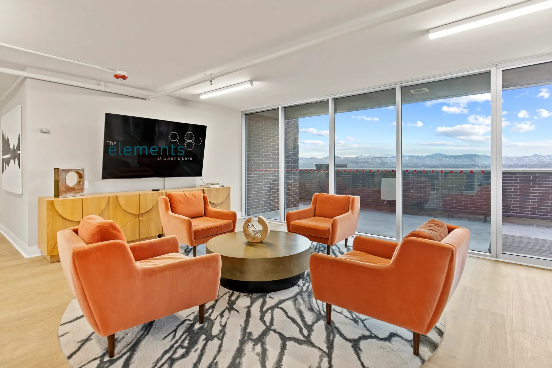 Lounge area with orange chairs, coffee table, and a TV displaying the property logo.
