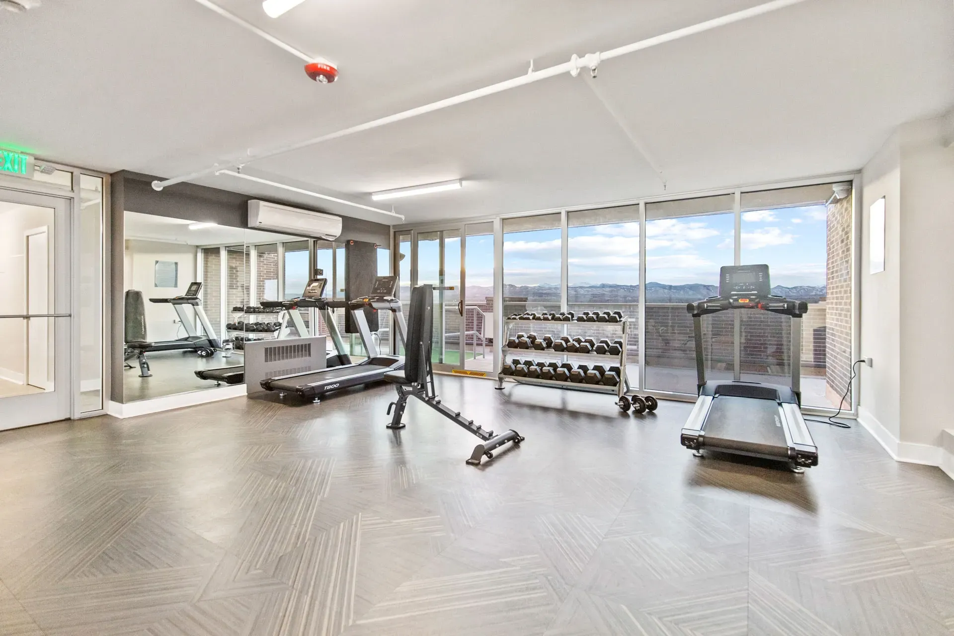 Gym with treadmills, dumbbells, and a weight bench, featuring large windows with mountain views.
