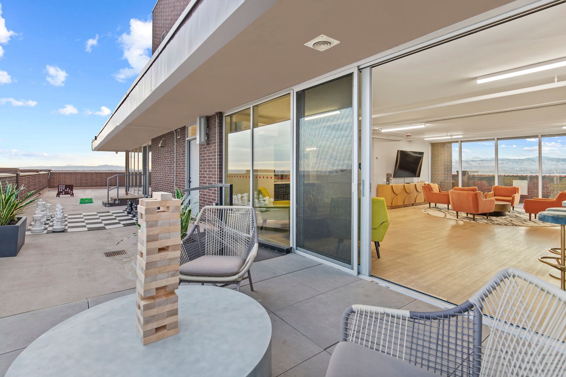Rooftop patio with wicker chairs, round table, and sliding doors opening to a bright modern living room