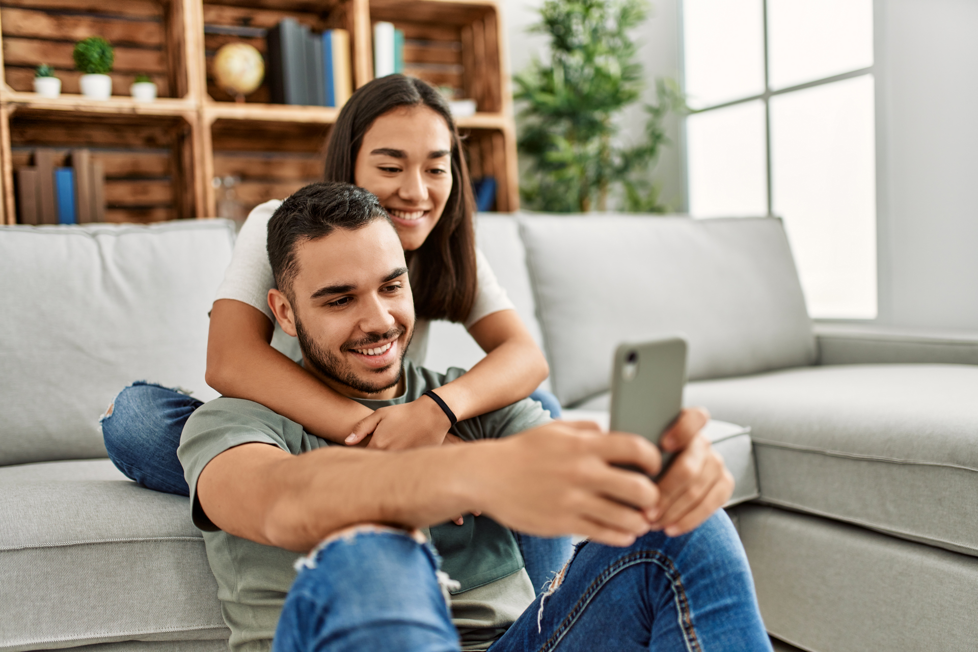 Smiling couple on a couch taking a selfie with a smartphone in a bright living room