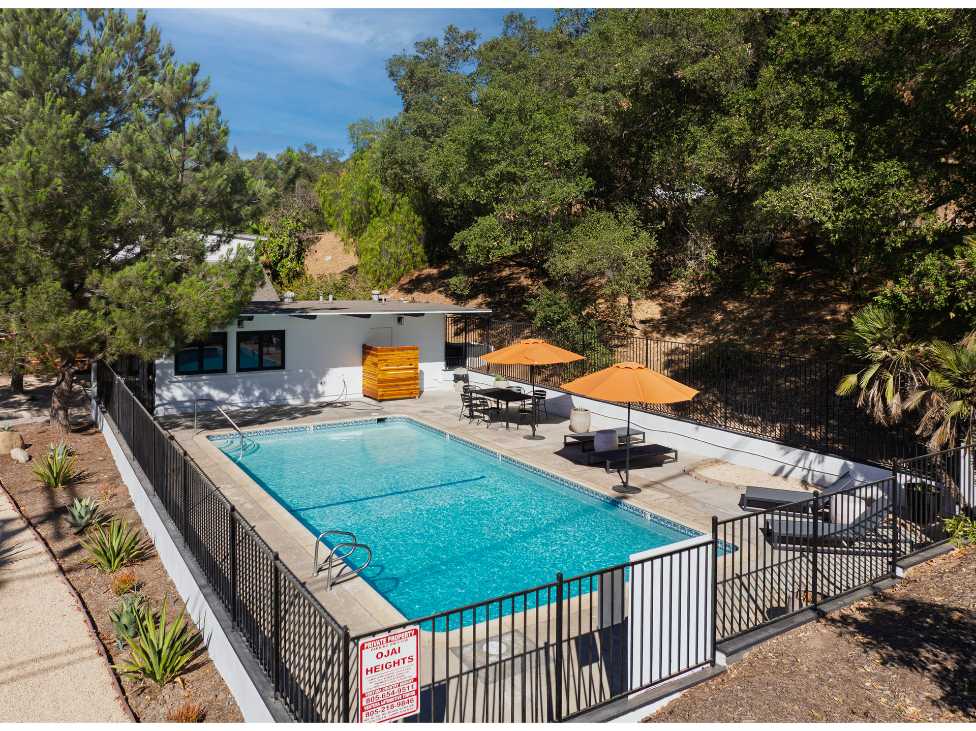 Outdoor swimming pool with orange umbrellas and lounge chairs beside a small building and trees