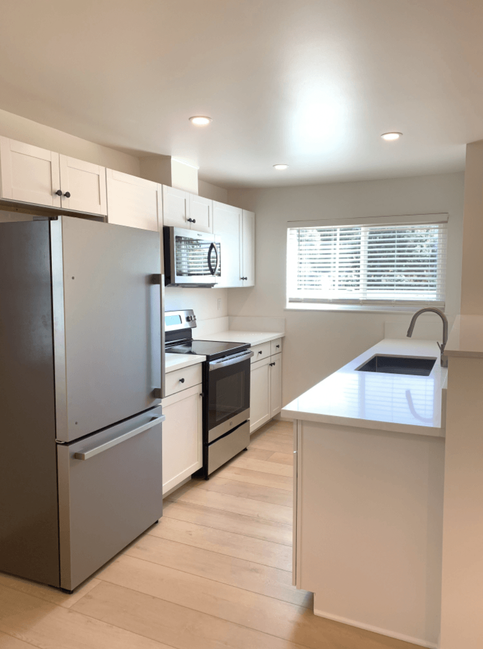 Bright modern kitchen with white cabinets, stainless fridge, island, and window blinds.