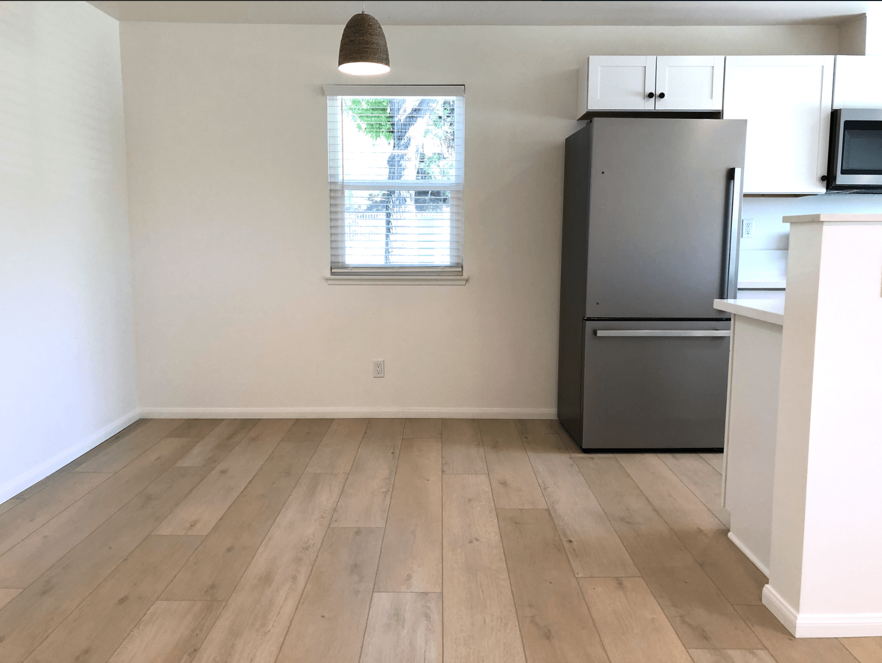 Empty modern kitchen and dining area with light wood floors, white walls, and a stainless steel refrigerator.