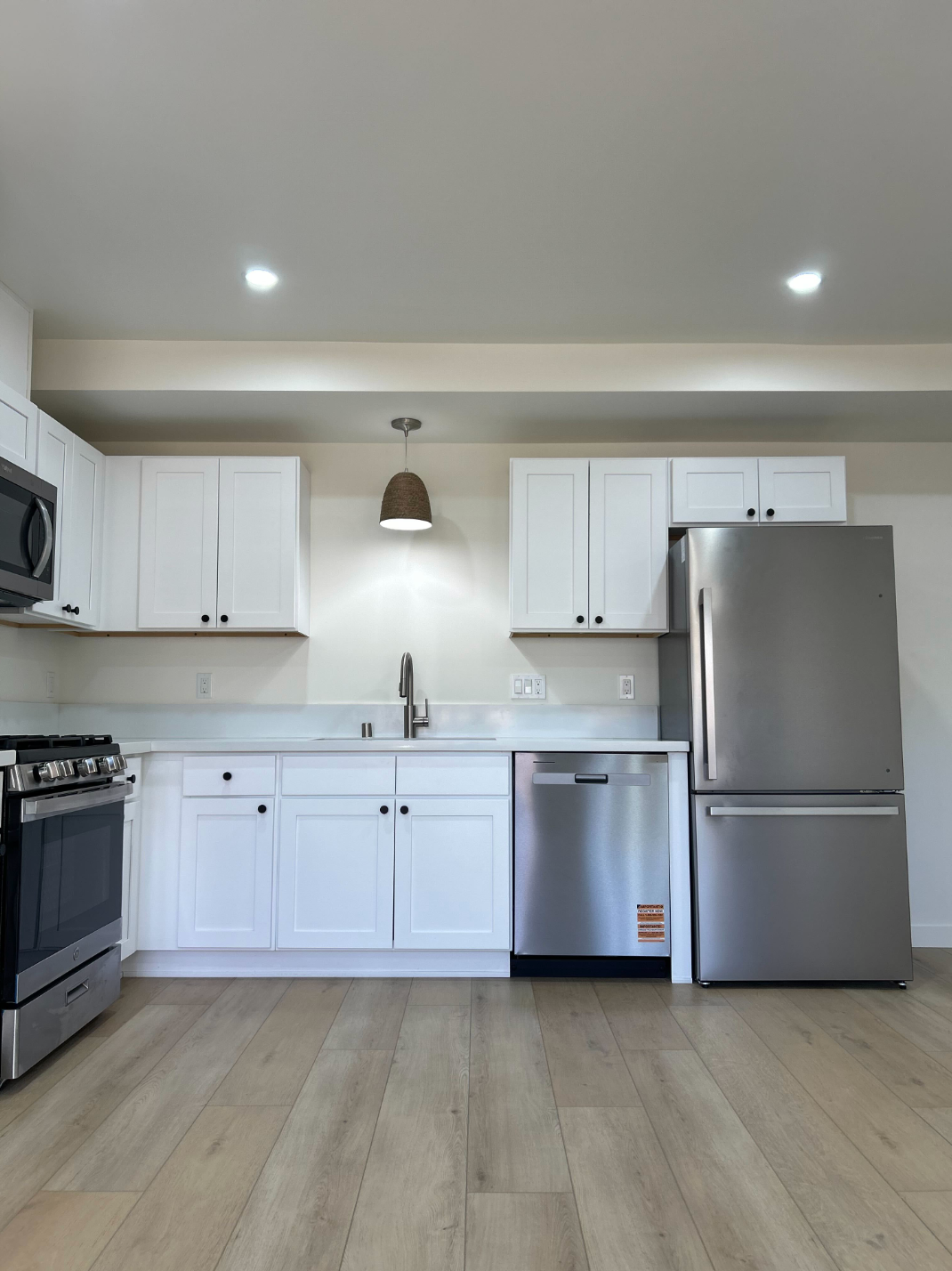 Bright modern kitchen with white cabinets, stainless steel appliances, and light wood flooring