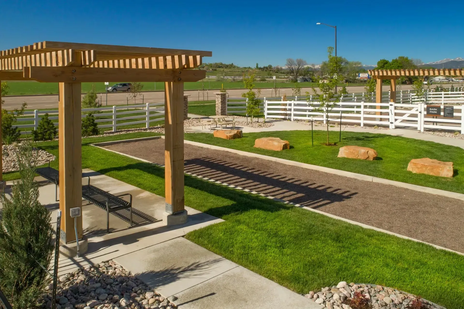 Outdoor dog park area with pergolas, benches, and a white fenced enclosure.
