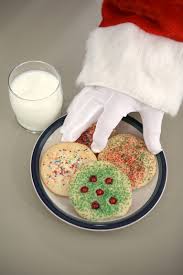 Call Ahead santa claus is reaching for a plate of cookies and a glass of milk .