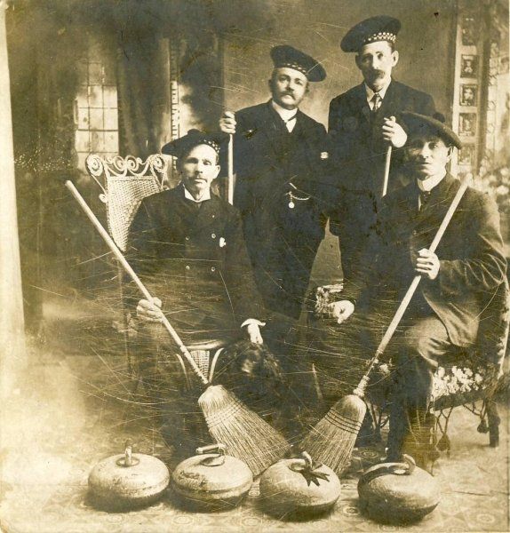 A black and white photo of four men holding brooms and curling rocks