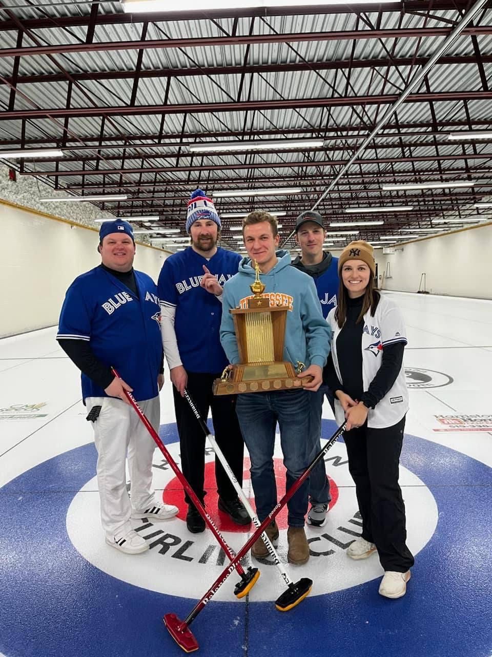A group of people standing on a curling rink holding a trophy