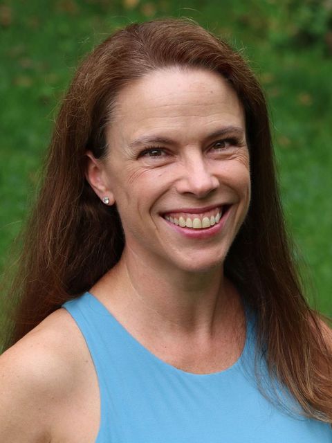 a woman with long brown hair is smiling for the camera while wearing a blue tank top .