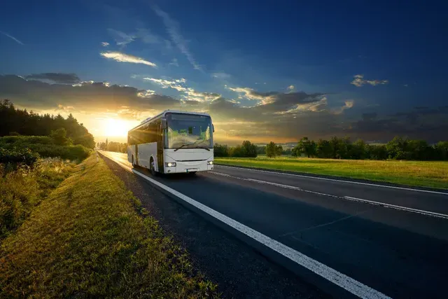 Camioneta blanca circulando por una autopista al atardecer con luz dorada y cielo nublado.