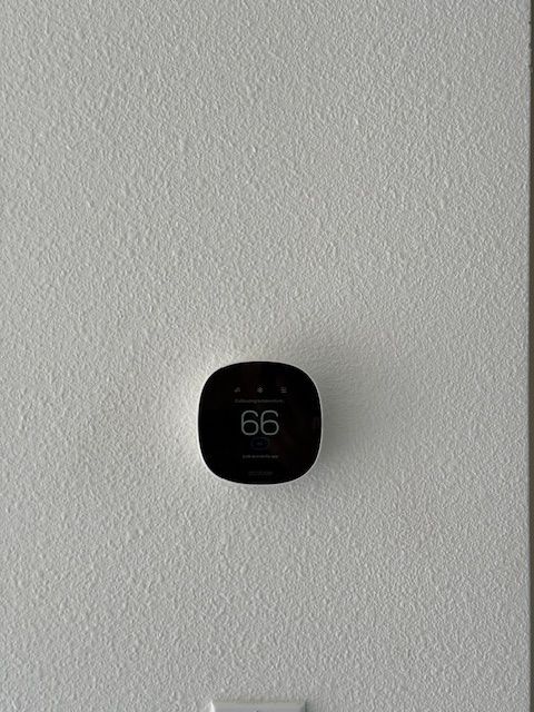 Smart thermostat on a textured white wall, displaying 66 degrees.