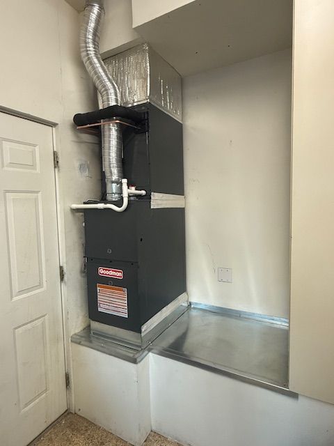 Furnace installation in a utility room with metal ducting, door, and a metal base.
