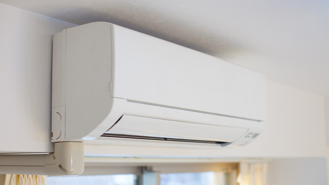 White wall-mounted air conditioning unit, with a white drainage pipe, indoors.