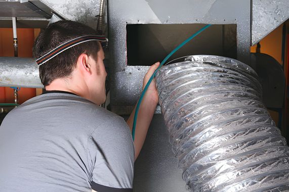 Silver HVAC ductwork running across a ceiling with blue lighting.