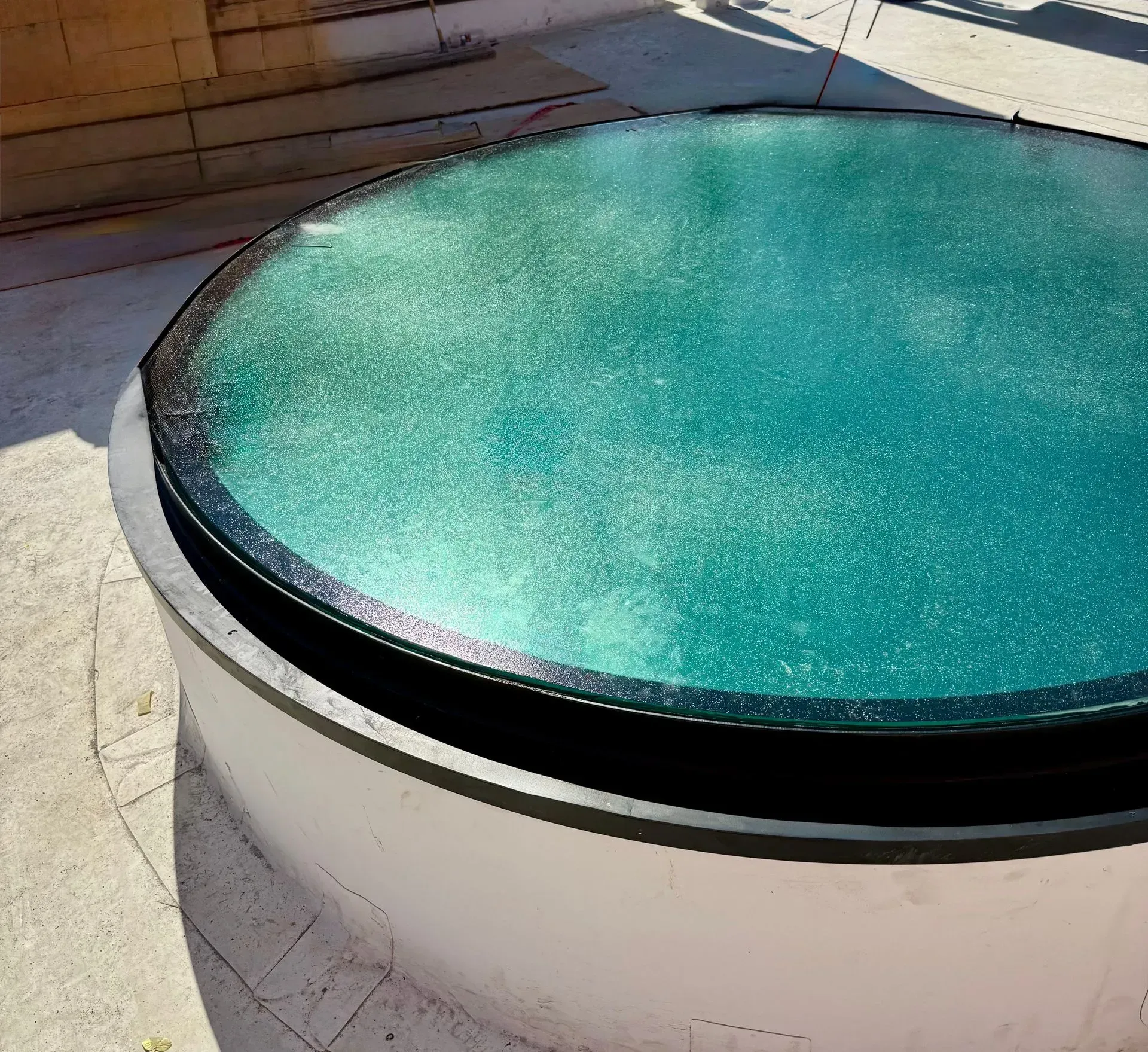 Round turquoise pool or spa with a black rim in a sunlit concrete patio area