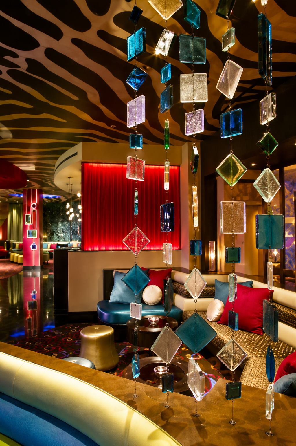 Stylish lounge with hanging glass cubes, red wall, patterned ceiling, and colorful seating