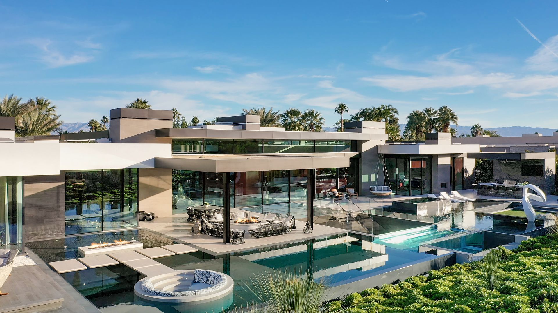 Modern luxury house with glass walls, pool, and patio overlooking a landscaped hillside view