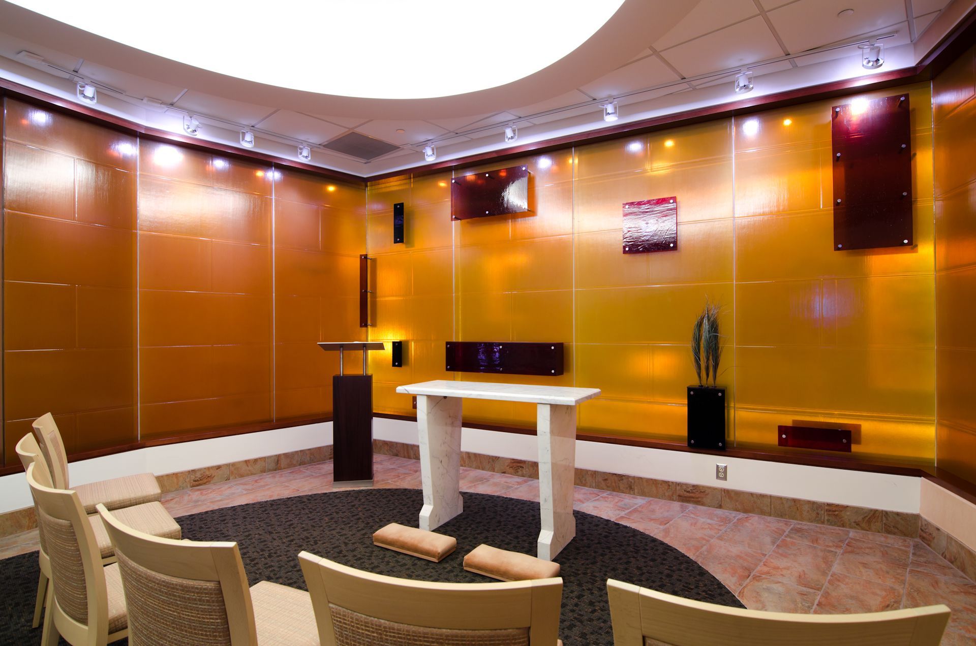 Modern conference room with curved orange walls, podium, and white tables facing a small stage