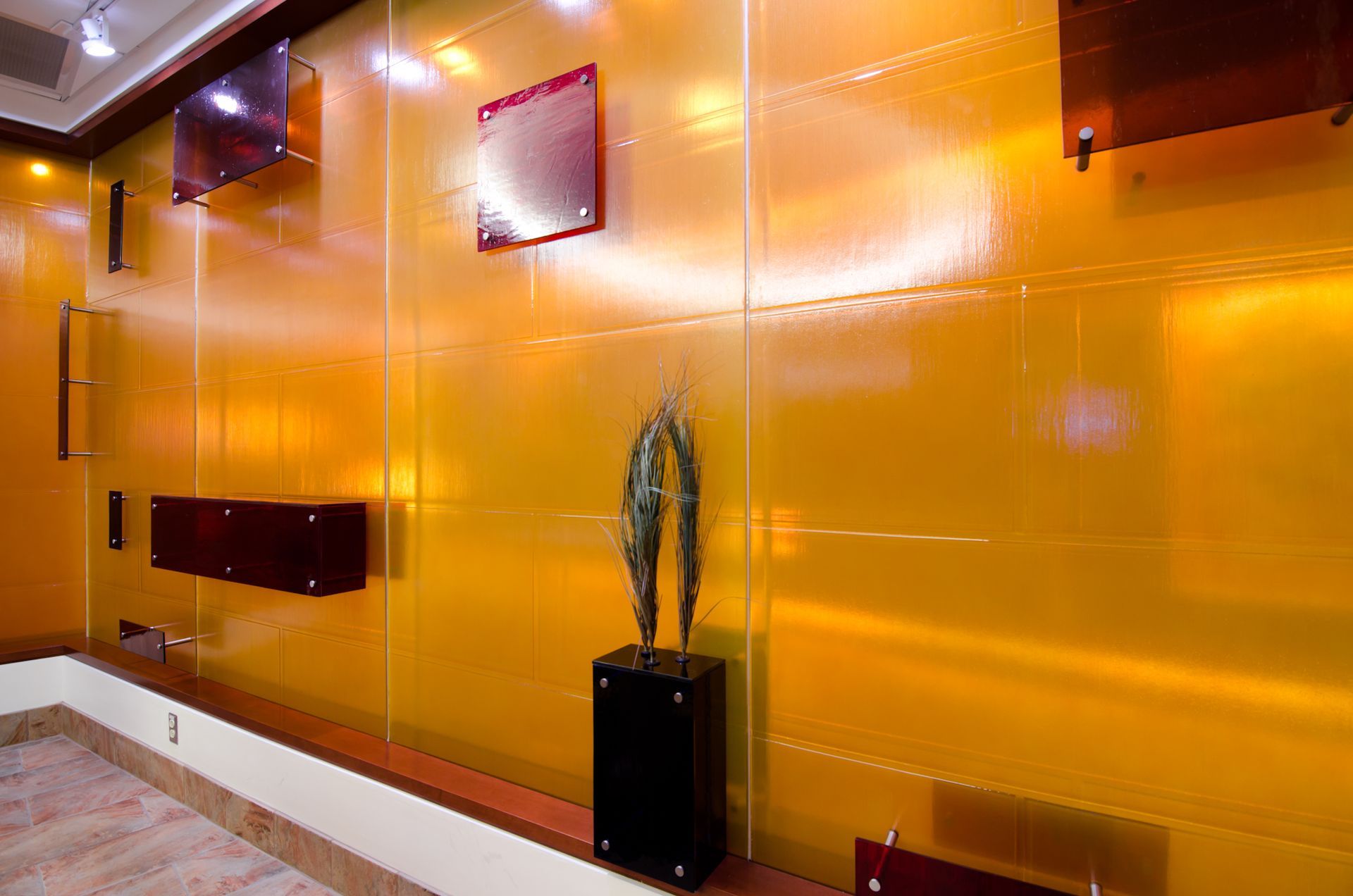 Orange glass-paneled wall with square wall lights and a black plant stand in a modern lobby