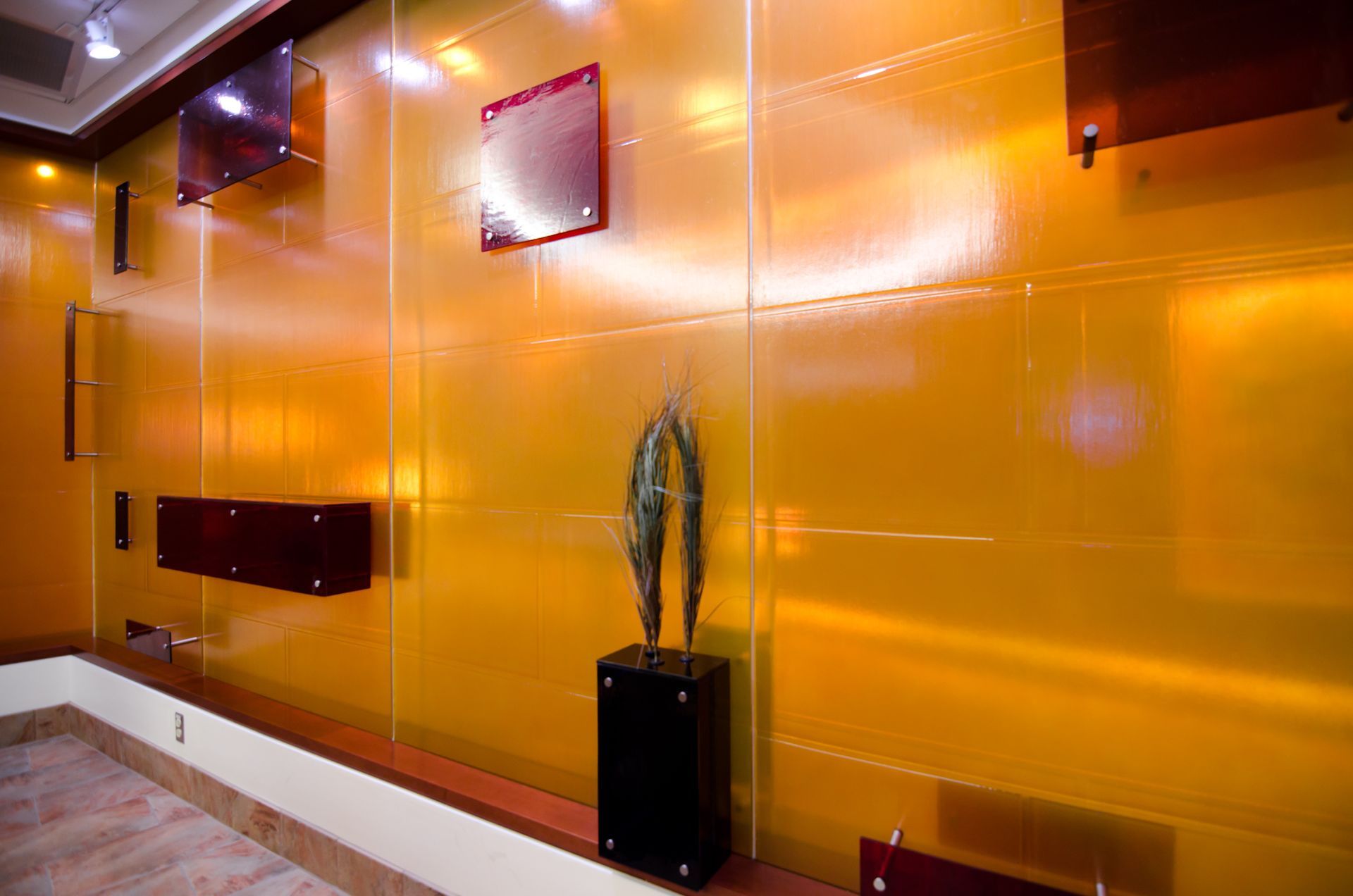 Modern lobby wall with glossy orange panels, recessed lighting, and a potted plant on a black pedestal.