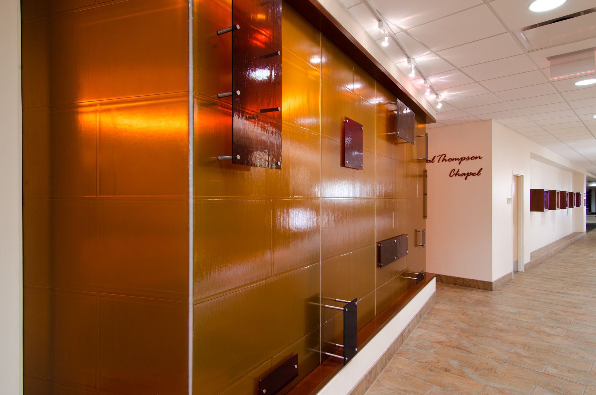 Modern office hallway with glossy copper wall panels and beige carpeted floor