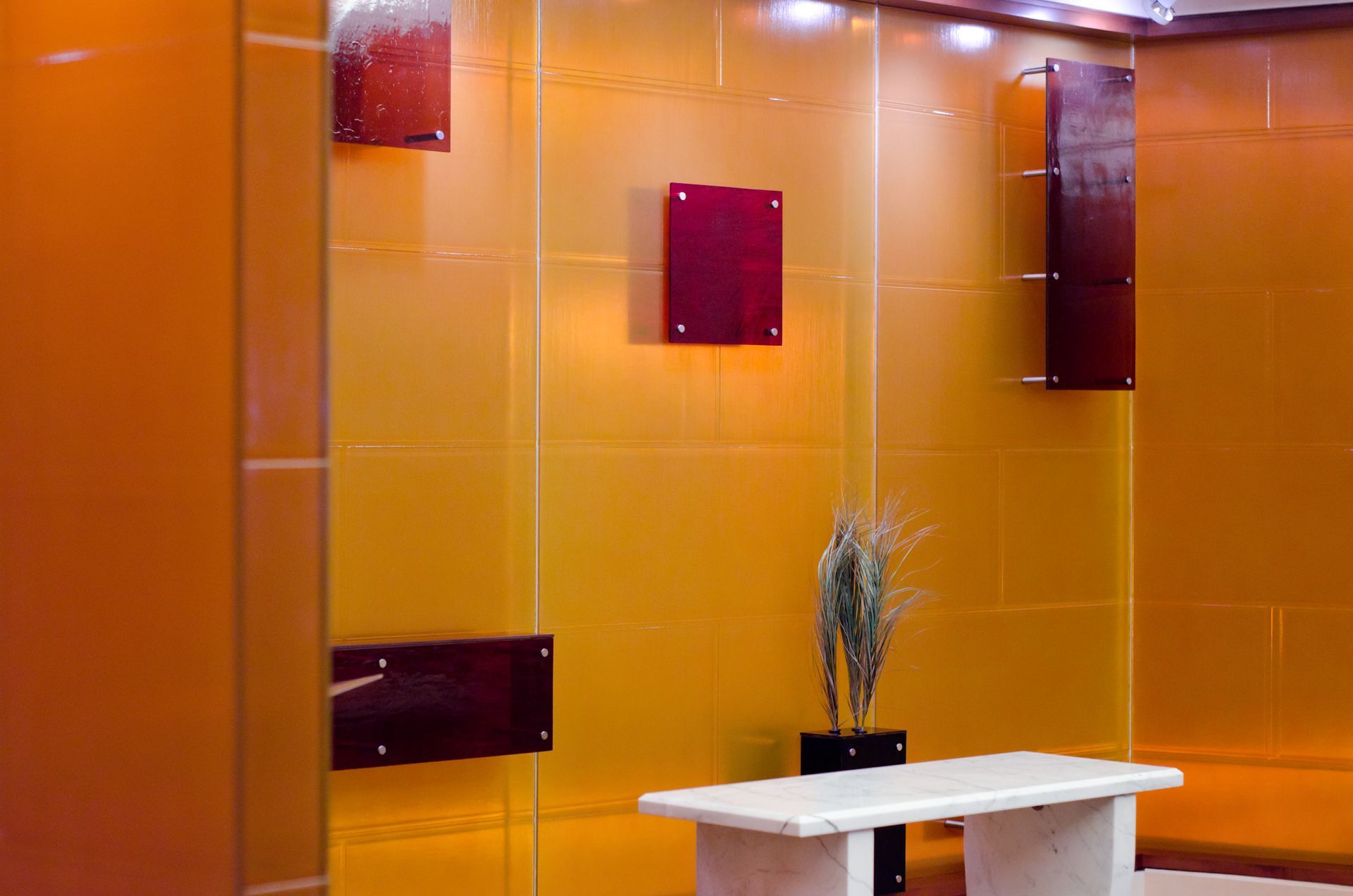 Orange tiled wall with burgundy accents and a small white table holding a vase of dried plants.