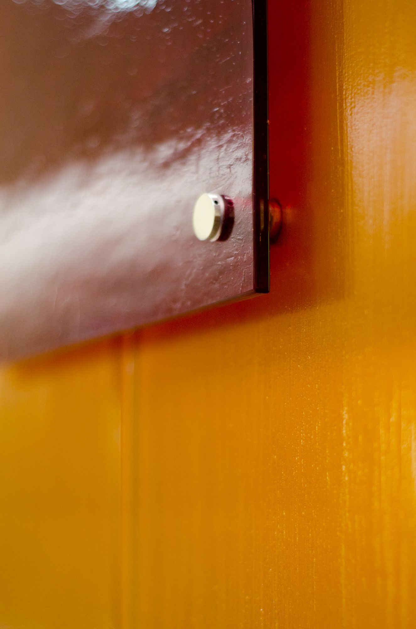 Close-up of a brown cabinet door on an orange wall, with a small white knob.