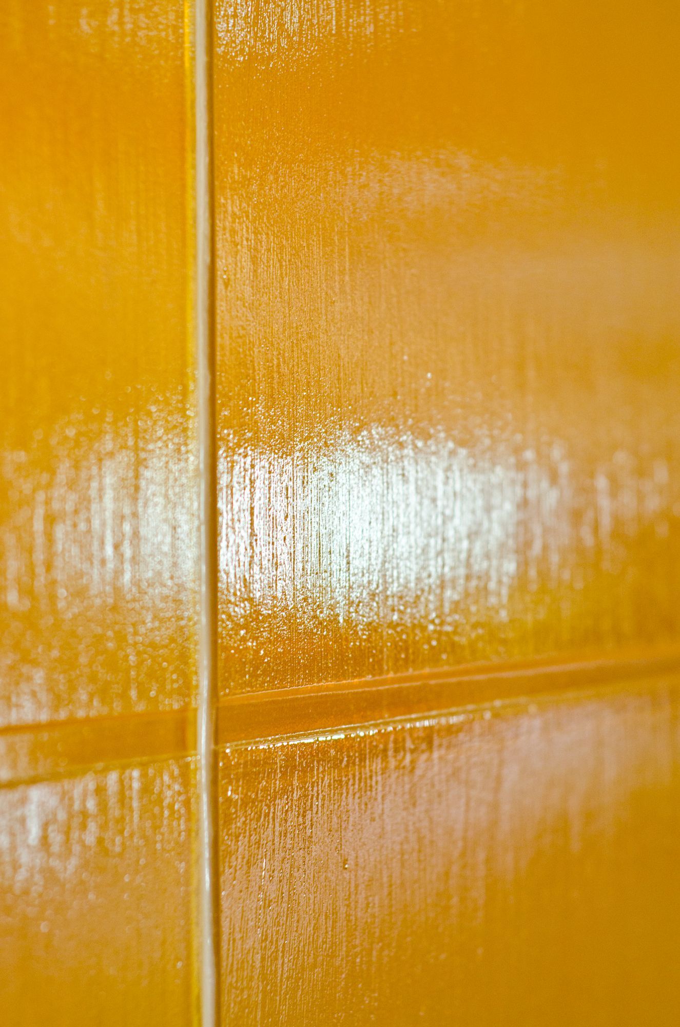 Close-up of a glossy orange wall with a vertical seam and bright white reflection