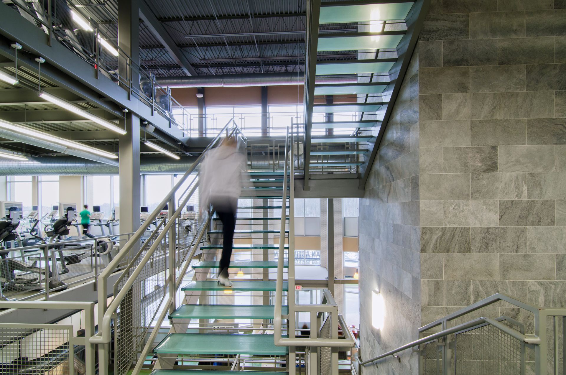 Person walking up glass stairs in a modern office interior with metal railings and open ceiling.