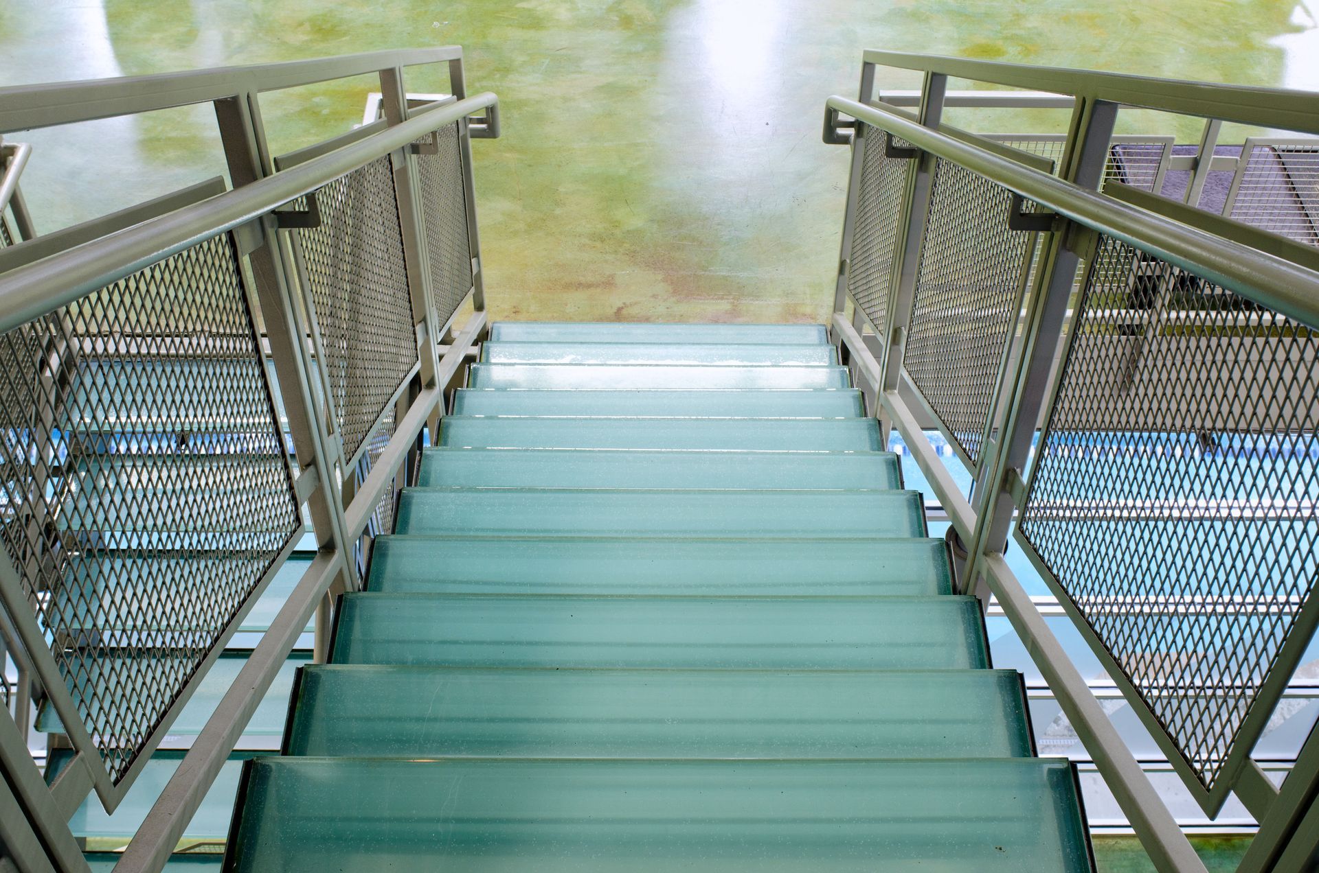 Stairs leading down to a calm body of water, flanked by metal railings and mesh sides
