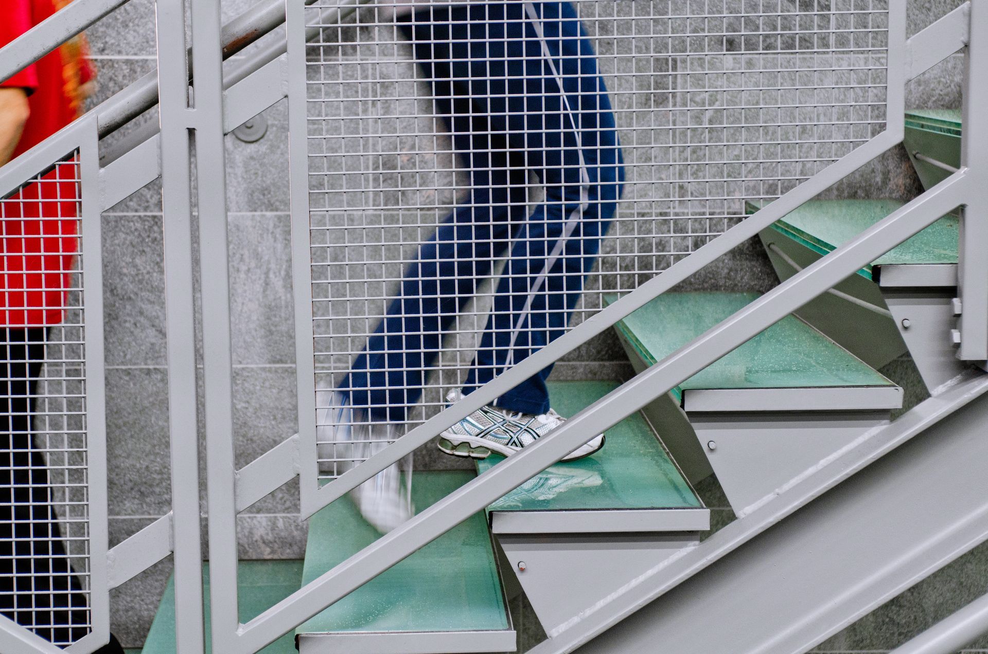 People ascending a metal staircase with green steps and white railings, one in blue jeans visible.