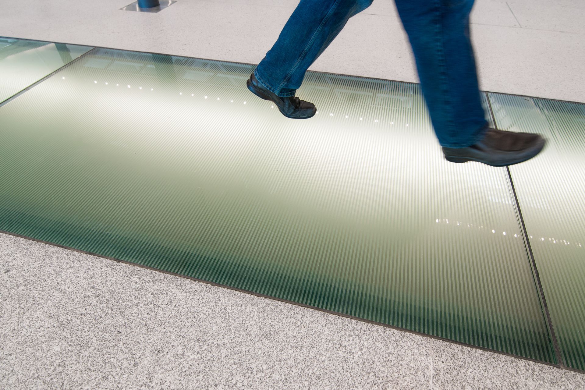 Person walking on a glass floor with a green-lit panel beneath them