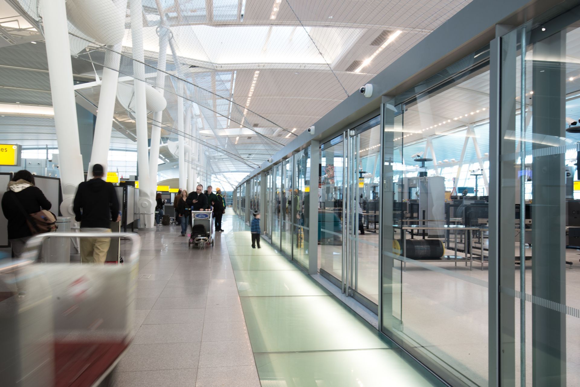 Bright airport concourse with travelers walking beside glass-walled shops and check-in counters
