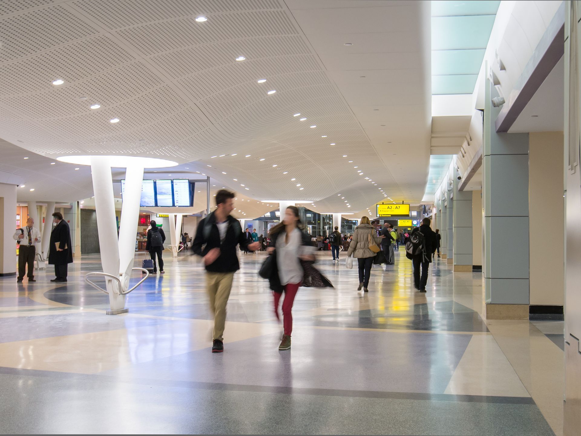 Busy airport concourse with travelers walking under a bright, curved ceiling.