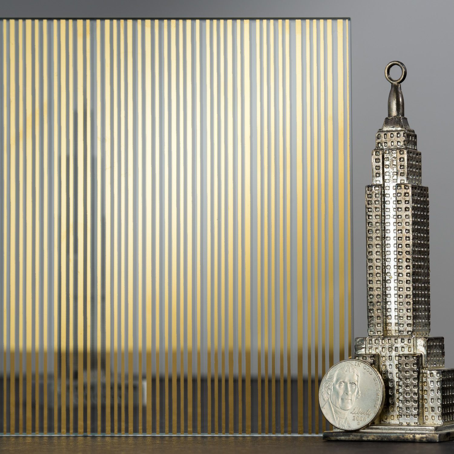 Glass panel with gold stripes, beside a silver Empire State Building statue and coin.