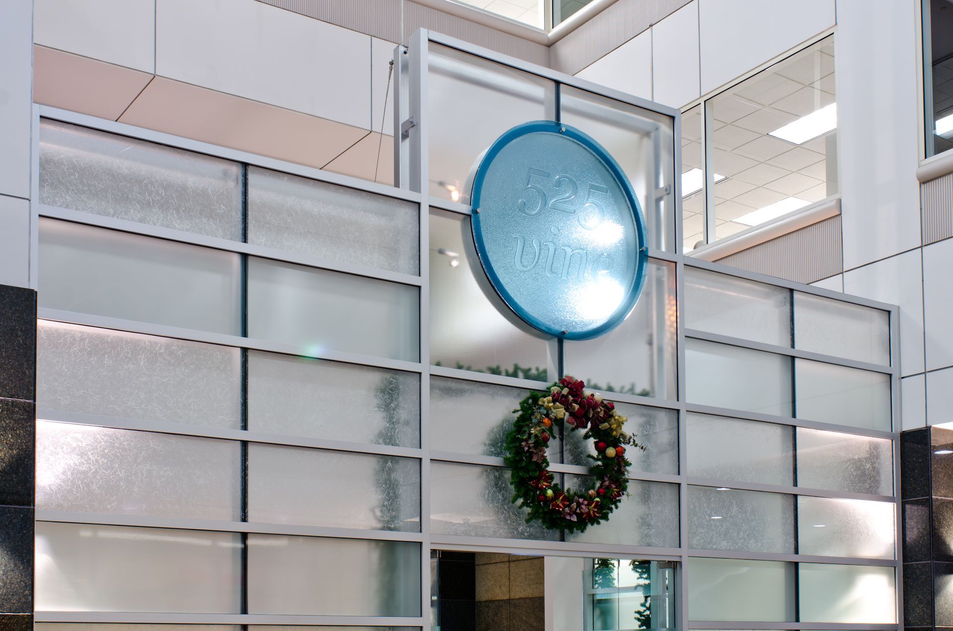 Glass wall with a large blue circular ornament above a holiday wreath in a bright atrium