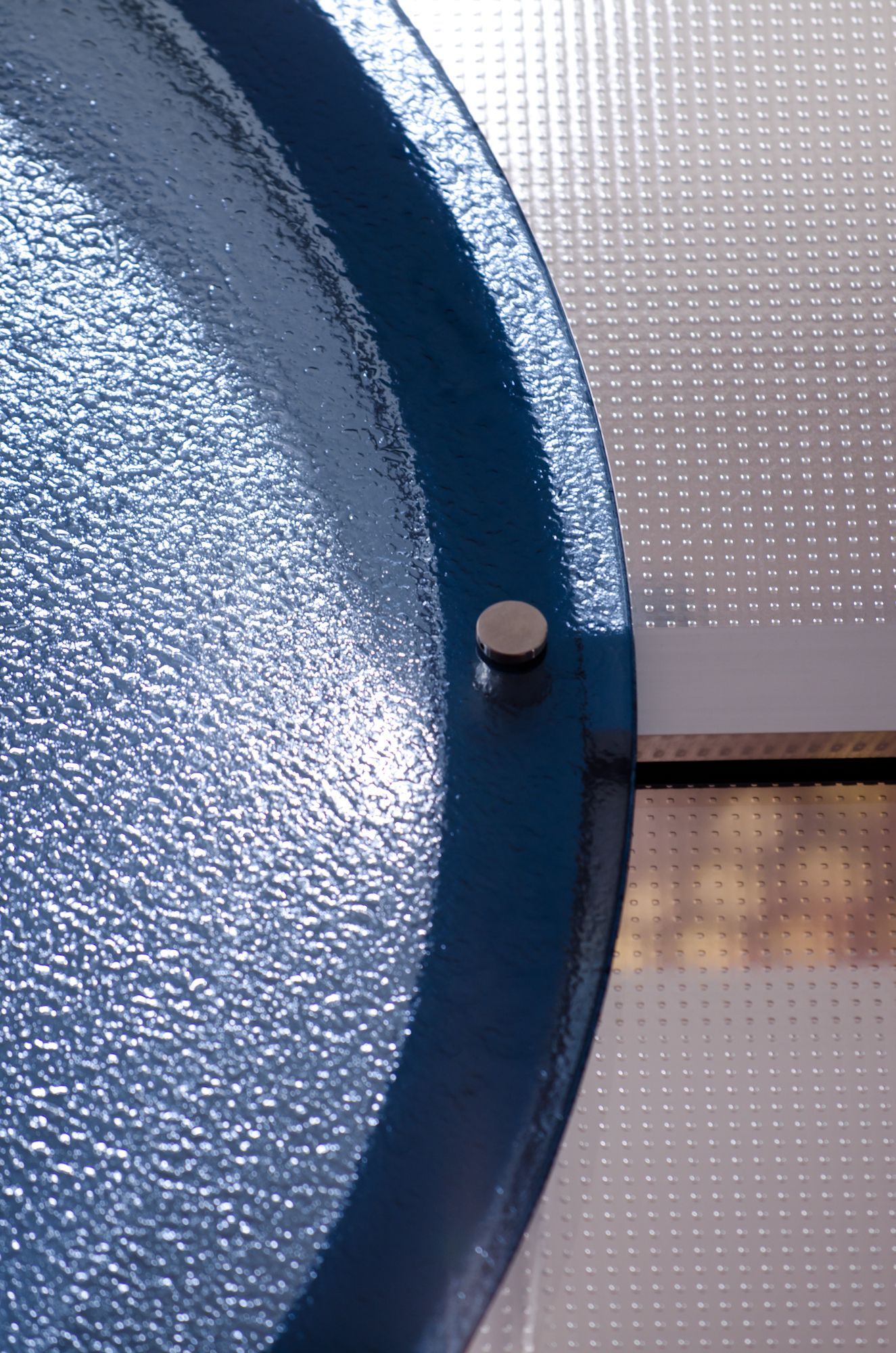 Blue textured circular object with a small silver knob beside a dotted metal surface.