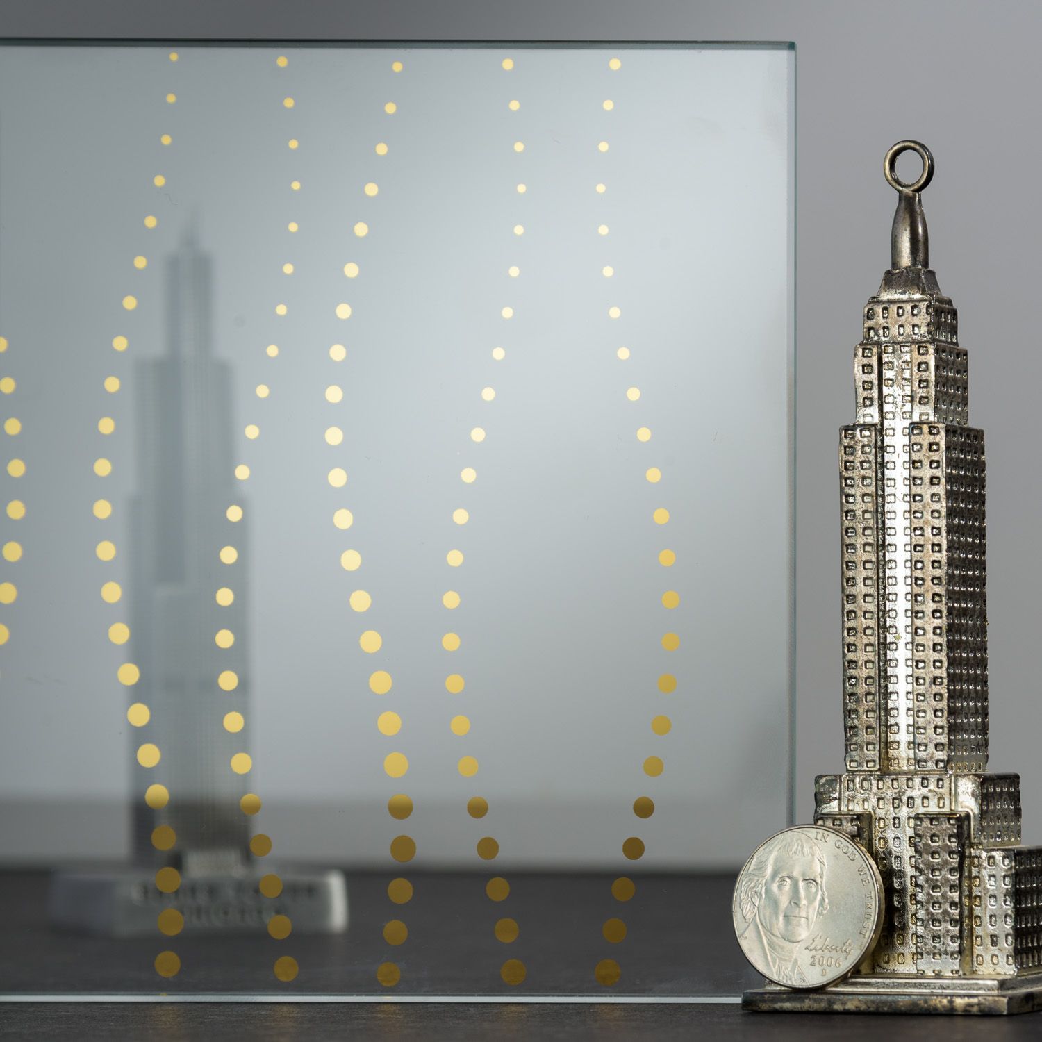 Silver Empire State Building figurine with a coin, in front of a mirror with a gold dot pattern.