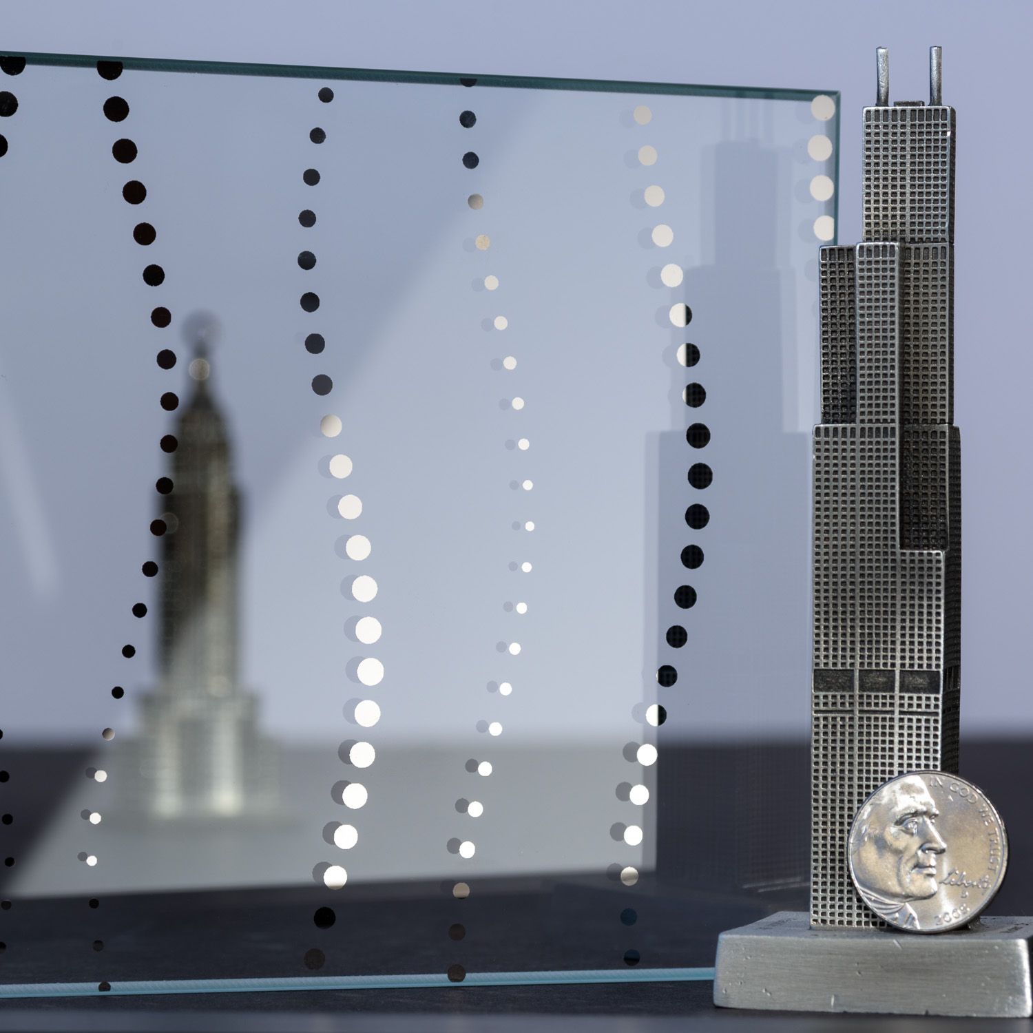 A glass pane with a dotted design stands before a miniature skyscraper and a coin.