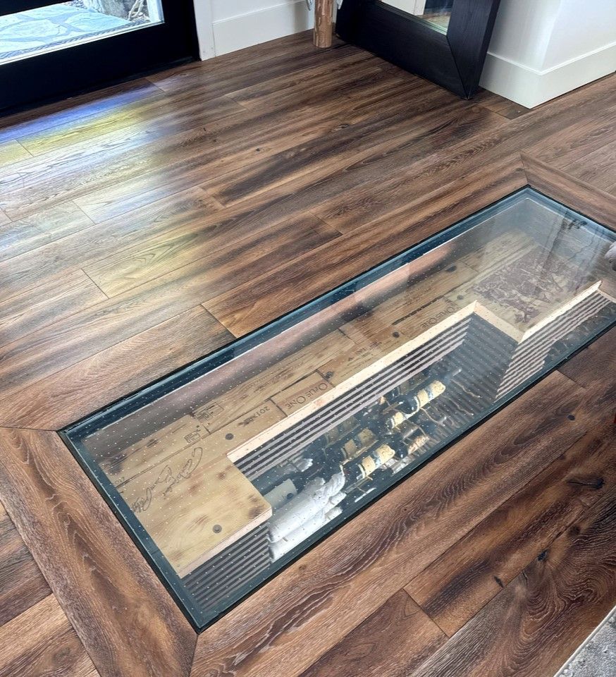 Glass floor panel revealing a wine cellar below, surrounded by wood flooring.
