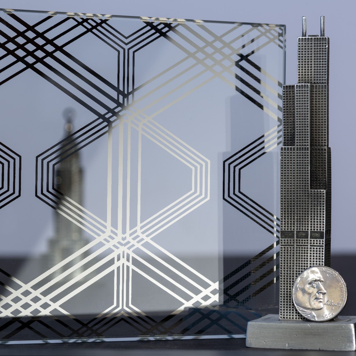 A metallic model of Willis Tower stands beside a patterned glass pane and a coin.