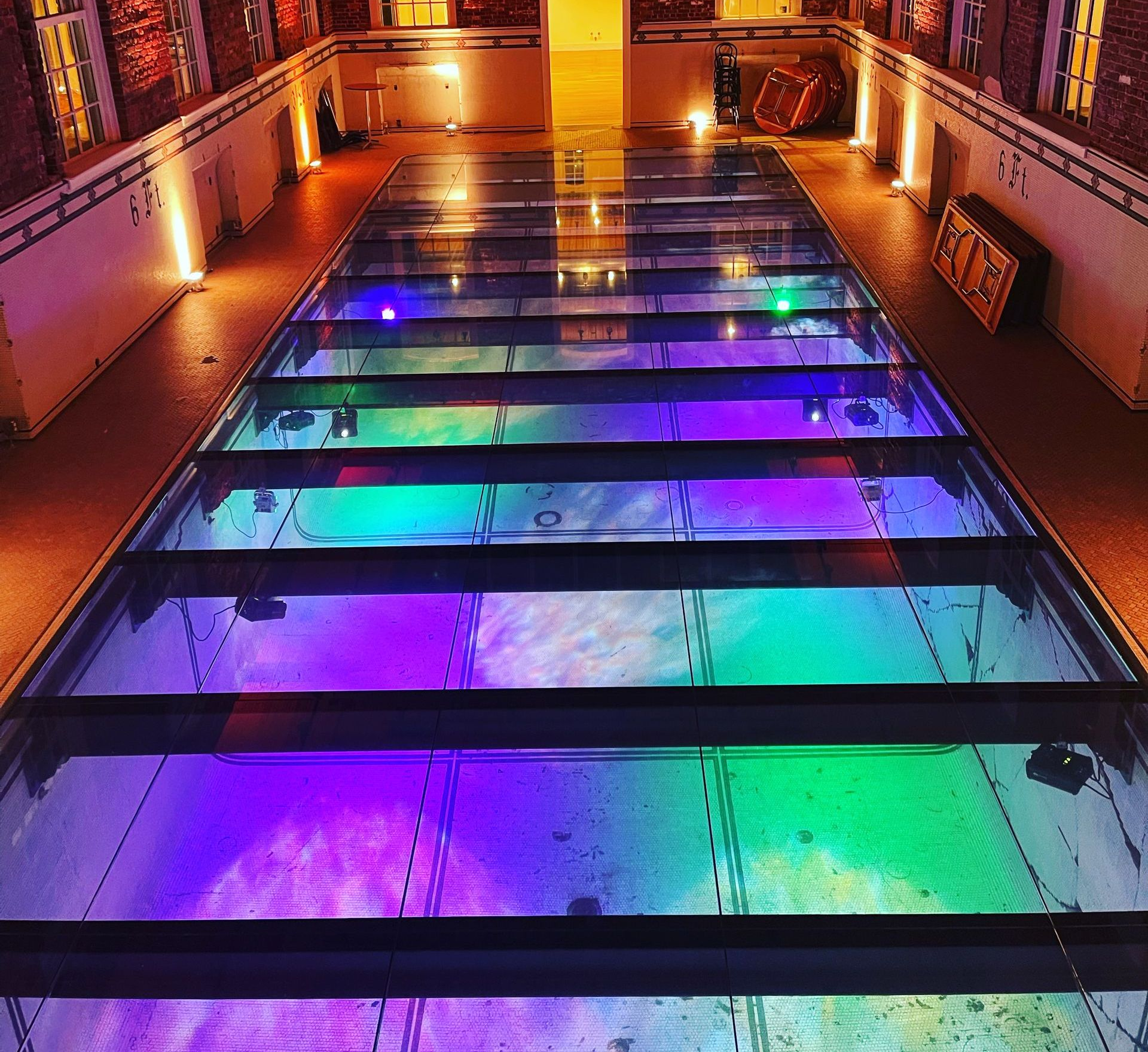 Colorful illuminated glass floor panels in a dimly lit walkway with purple, blue, and green lights
